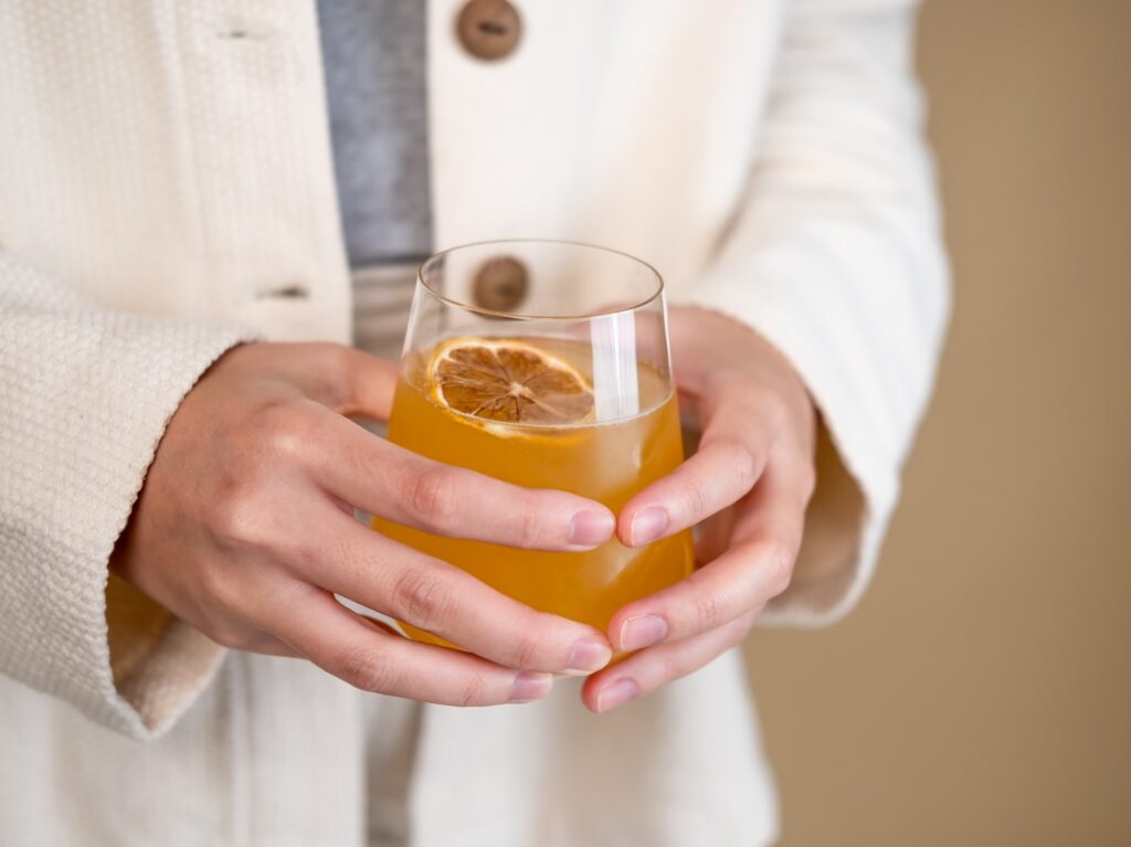person holding clear drinking glass with orange liquid