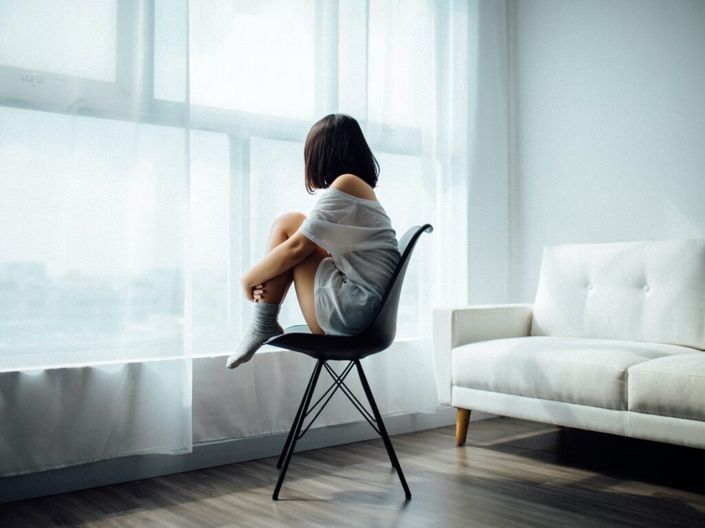 woman sitting on black chair in front of glass-panel window with white curtains